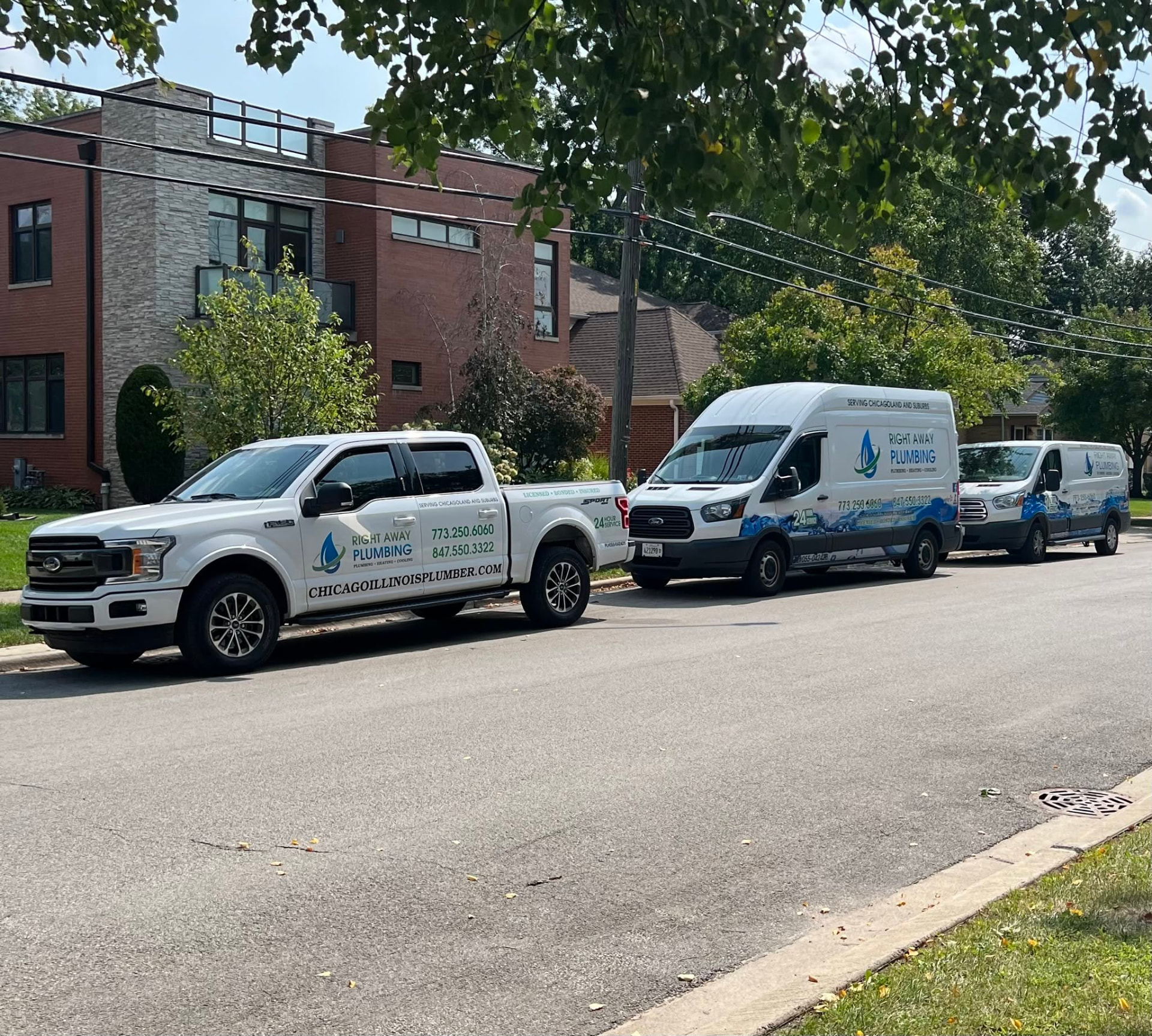 Three white Right Away Plumbing & HVAC service vehicles — a pickup truck and two vans — parked along a residential street, branded with the Right Away Plumbing, Heating and Cooling logo and phone numbers 773-250-6060 and 847-550-3322
