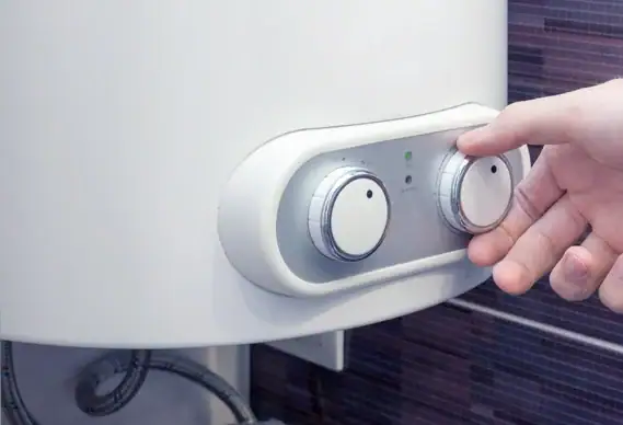 A hand adjusts a dial on a white water heater with two control knobs and indicator lights, mounted against a tiled wall—a common scene for plumbing Chicago or HVAC Chicago professionals.