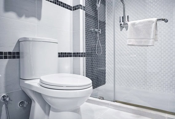 Modern bathroom in Chicago with a white toilet, glass shower enclosure, wall-mounted towel, and black-and-white tile accents—showcasing quality plumbing Chicago homeowners trust.