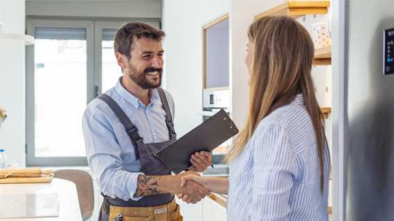 A smiling repairman holding a clipboard shakes hands with a woman in a bright, modern kitchen. Both appear friendly and professional, suggesting a successful HVAC Chicago service visit in IL.