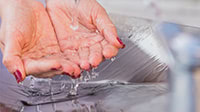 Close-up of a pair of hands with red nail polish cupped together under running water at a sink, highlighting the importance of reliable plumbing Chicago, IL.